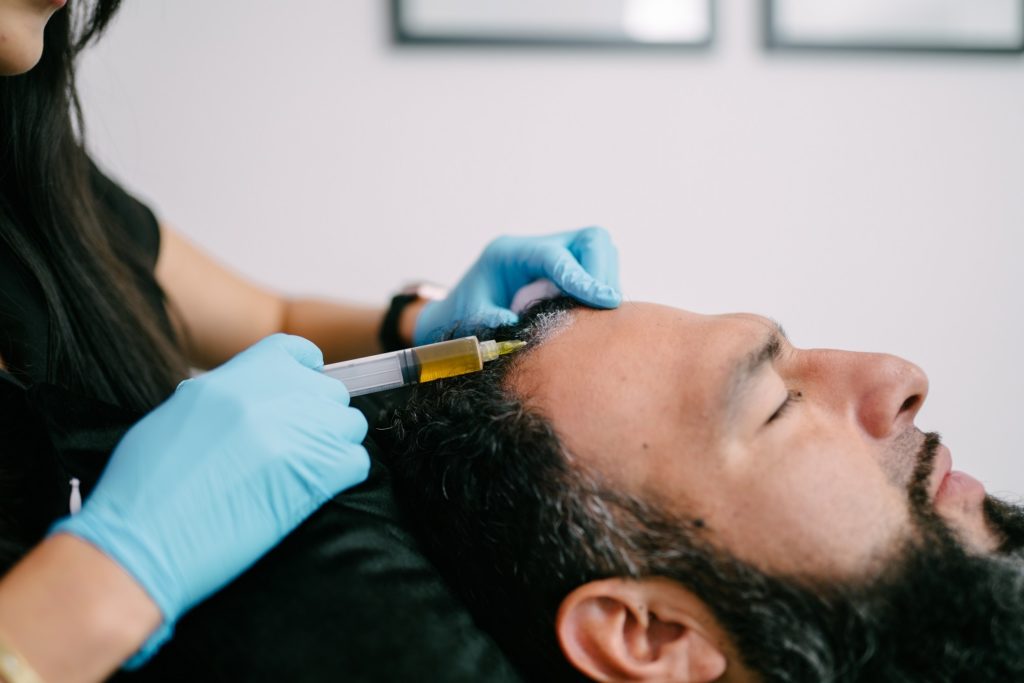 Cosmetologist holding syringe and man's head in hands Getting Hair Restoration treatment | Refined Aesthetics in Olmos Park, Texas